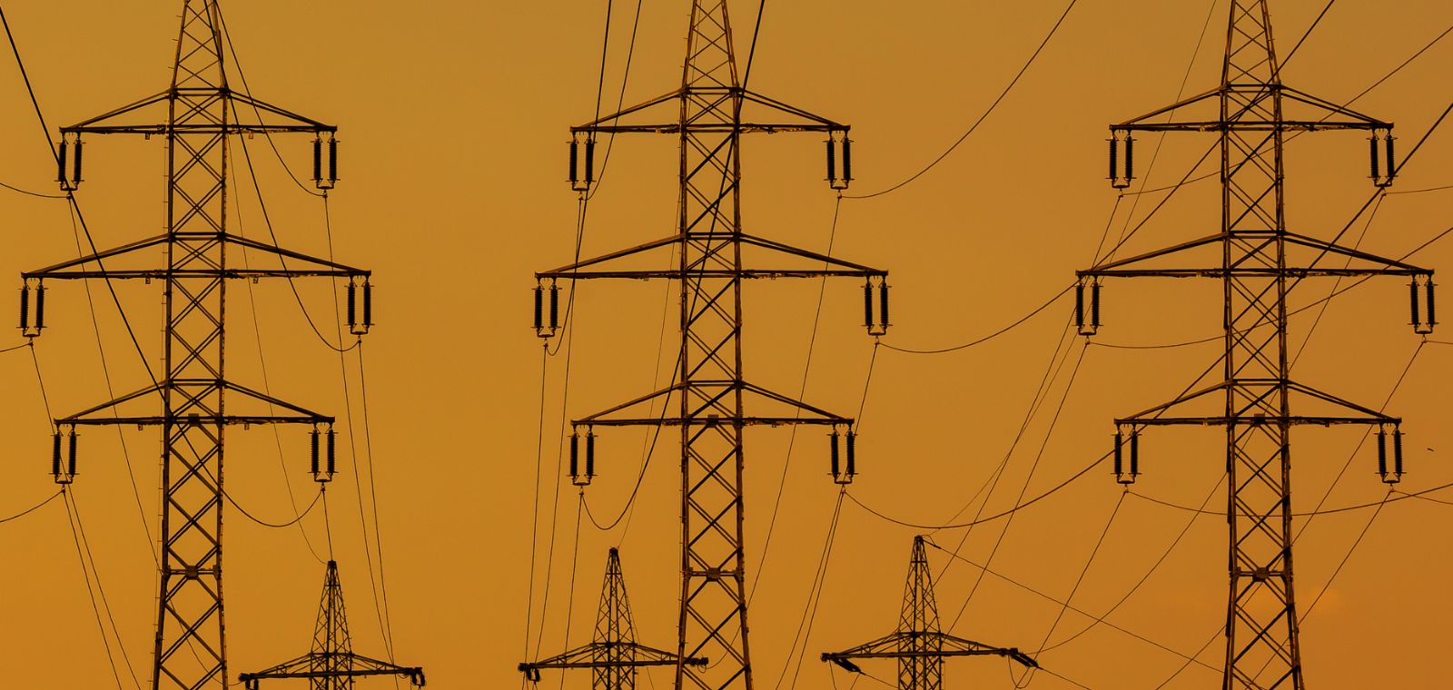 Electric powerline towers stand at attention as if in formation against a bleak pale red tint.  